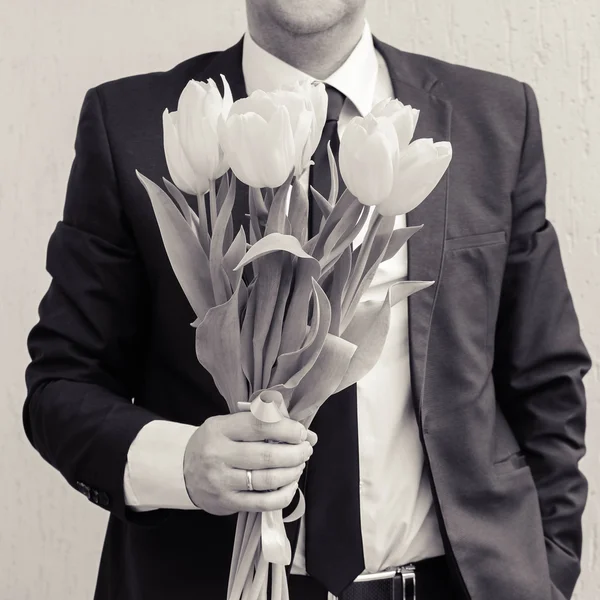 Мужчина в костюме бизнес, держит букет тюльпанов. Человек дает букет цветов. Черно-белый снимок — стоковое фото