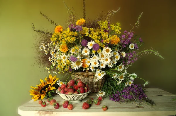 Still life with berries and flowers . Red , ripe strawberries and a bouquet of wildflowers and sunflowers . Стоковое Фото