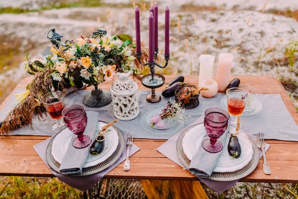 Деревянный стол подается на двоих, на столе есть композиции, цветы, свечи, столовые приборы и бокалы для вина Стоковое Изображение