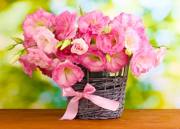Букет из эустомы цветов в плетеной вазе, на деревянном столе, на зеленом фоне Лицензионные Стоковые Фото